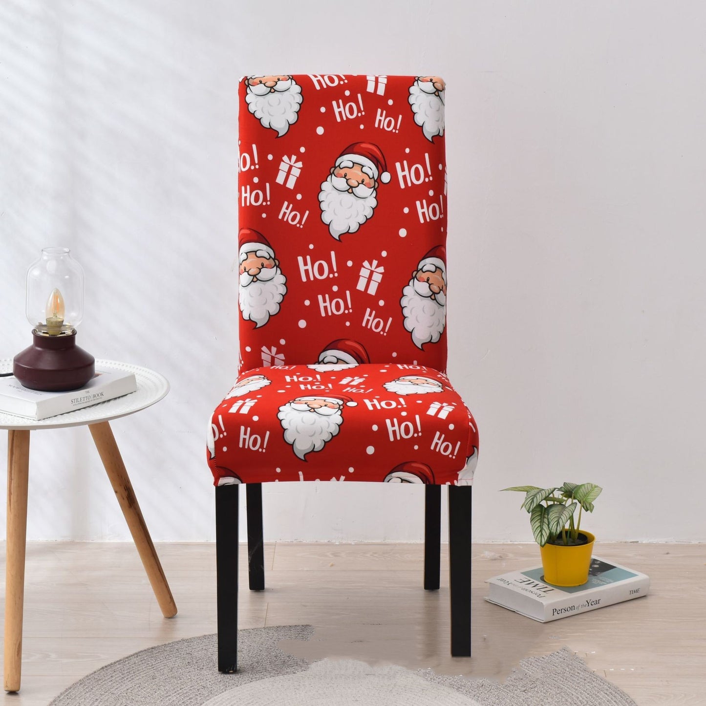 Festive red chair cover with vibrant Christmas-themed designs, including Santa Claus faces, white snowflakes, and the phrase 'Ho!' in bold white font. Features additional details like gift box illustrations with red ribbons. Snug fit for chairs with black legs, perfect for adding a cheerful holiday touch to your dining or living space. Ideal for Christmas home decorations and creating a warm, seasonal atmosphere.
