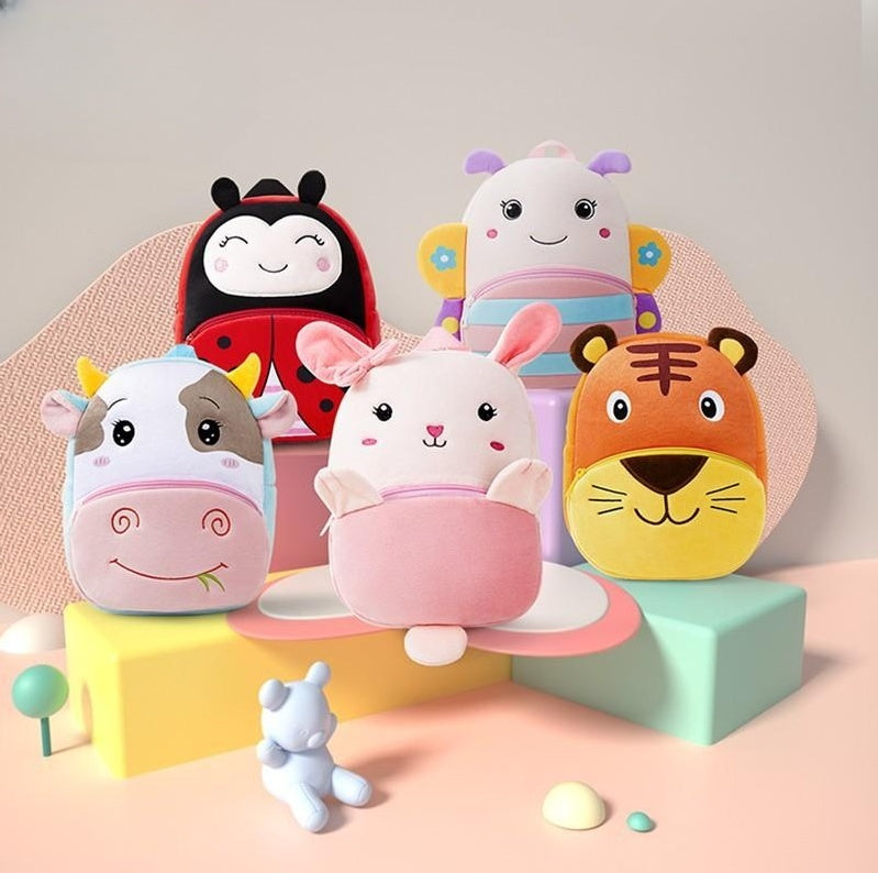 Plush children’s kindergarten backpacks featuring cute animal designs including a ladybug, cow, bunny, tiger, and butterfly, displayed on colorful blocks.