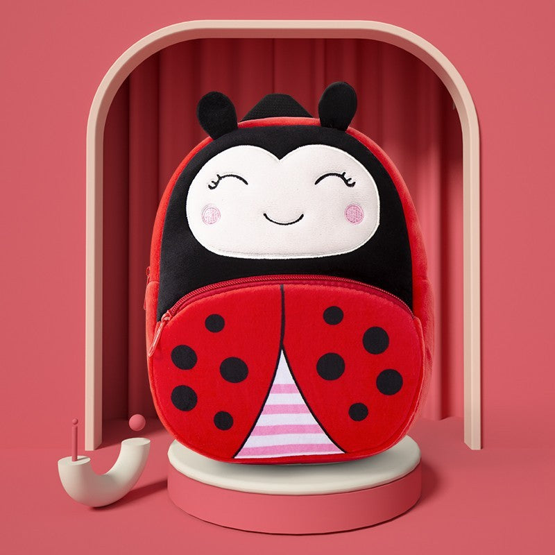 Plush children’s kindergarten backpacks featuring cute animal designs including a ladybug, cow, bunny, tiger, and butterfly, displayed on colorful blocks.