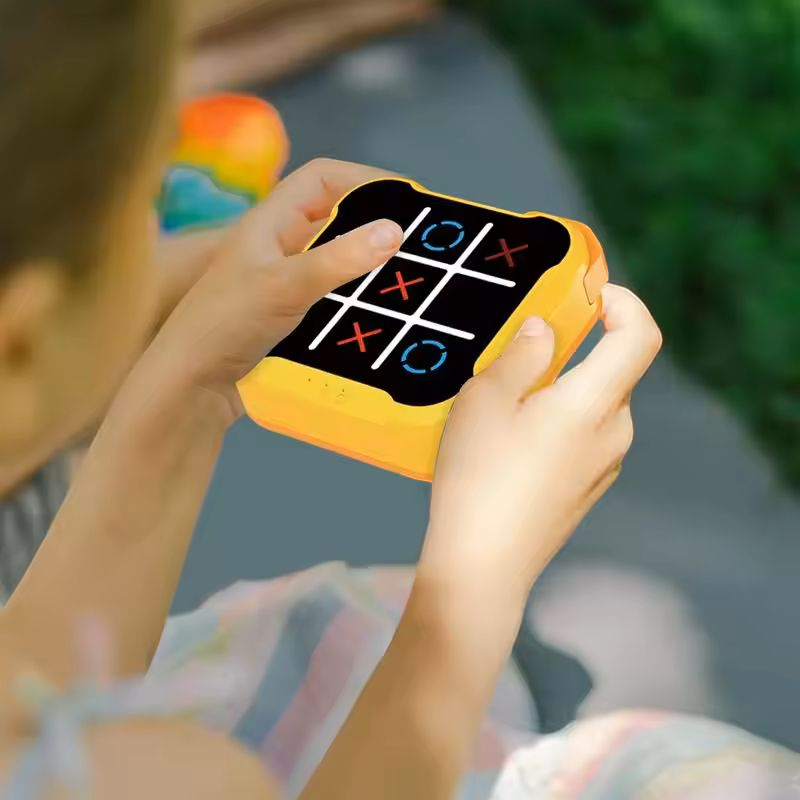 Ultimate Tic-Tac-Toe Showdown: Adult vs. Kid Challenge - A handheld electronic Tic-Tac-Toe game featuring a bright orange casing. The game screen displays a 3x3 grid with white lines, showcasing red X's and blue O's in various positions. The game is shown in two perspectives: a close-up of the game itself and a smaller image of hands holding and playing the game. Available in different colors.