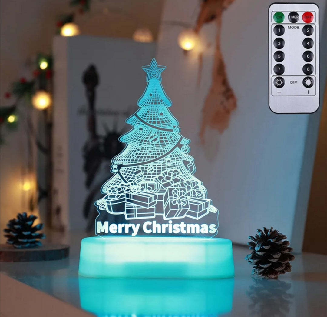 Illuminated Christmas LED lamps with a 'Merry Christmas' sign featuring reindeer antlers and a Christmas tree with presents underneath. The lamps glow warmly, set against a backdrop of a decorated Christmas tree with lights and ornaments. Pine branches and a pine cone add to the festive ambiance.