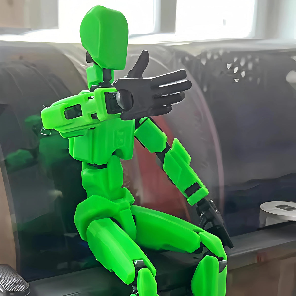 A bright green articulated 3D-printed robot arm or pose mannequin with black joint accents, sitting on a dark surface in an indoor setting.