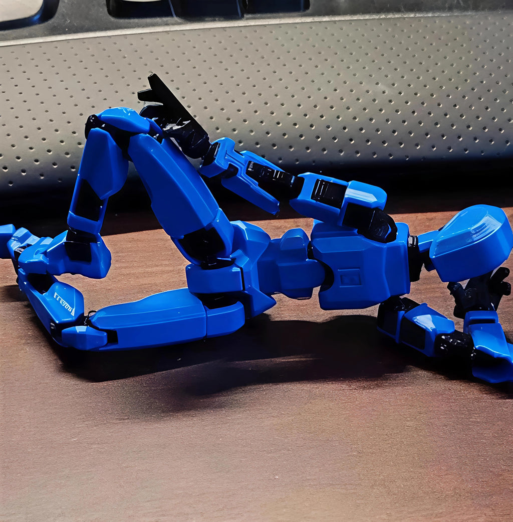 A blue and black articulated robot toy figure posed on a brown wooden surface in front of a gray perforated background.