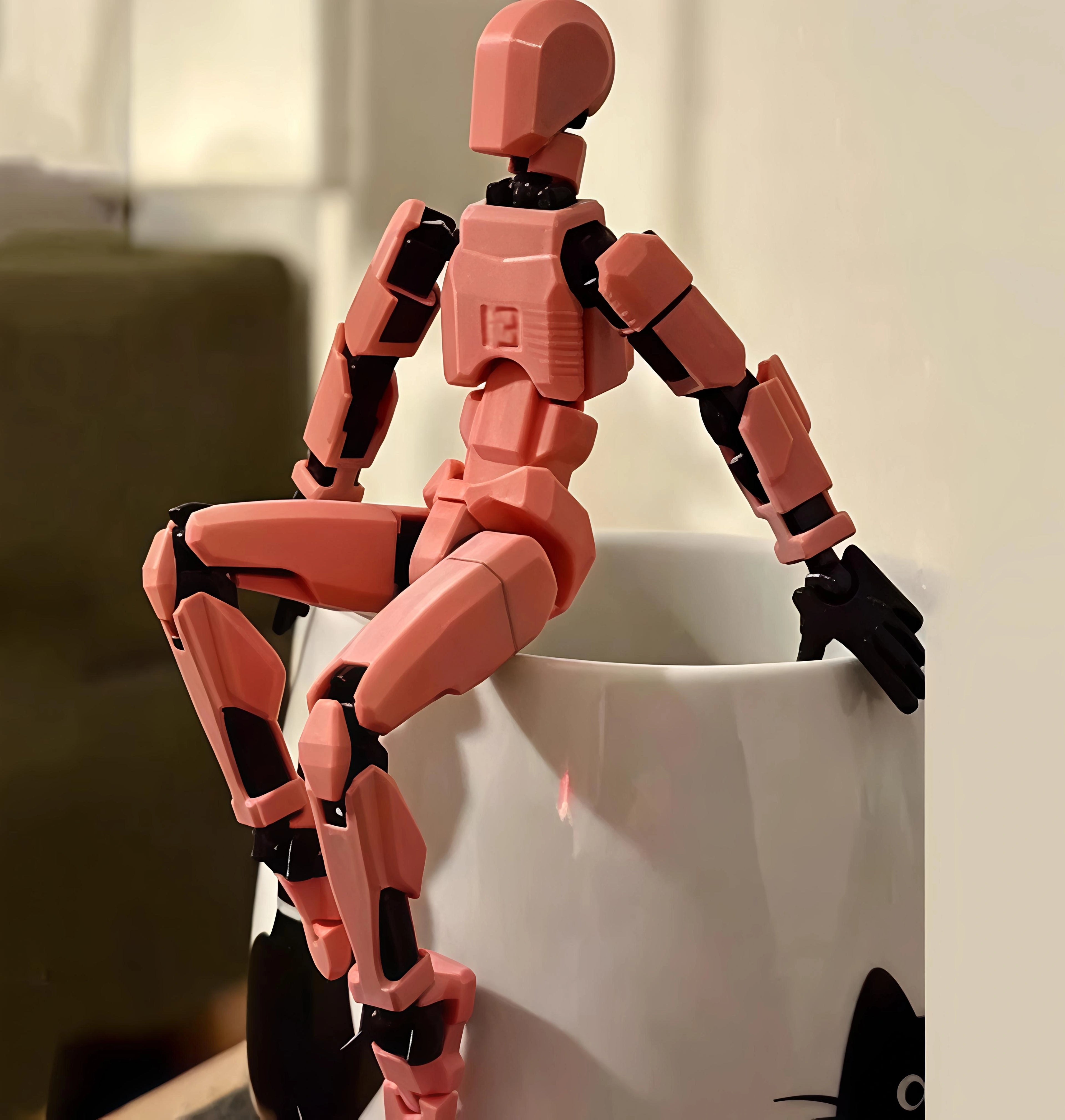 Pink robot toy leaning against a white mug with a blurred background