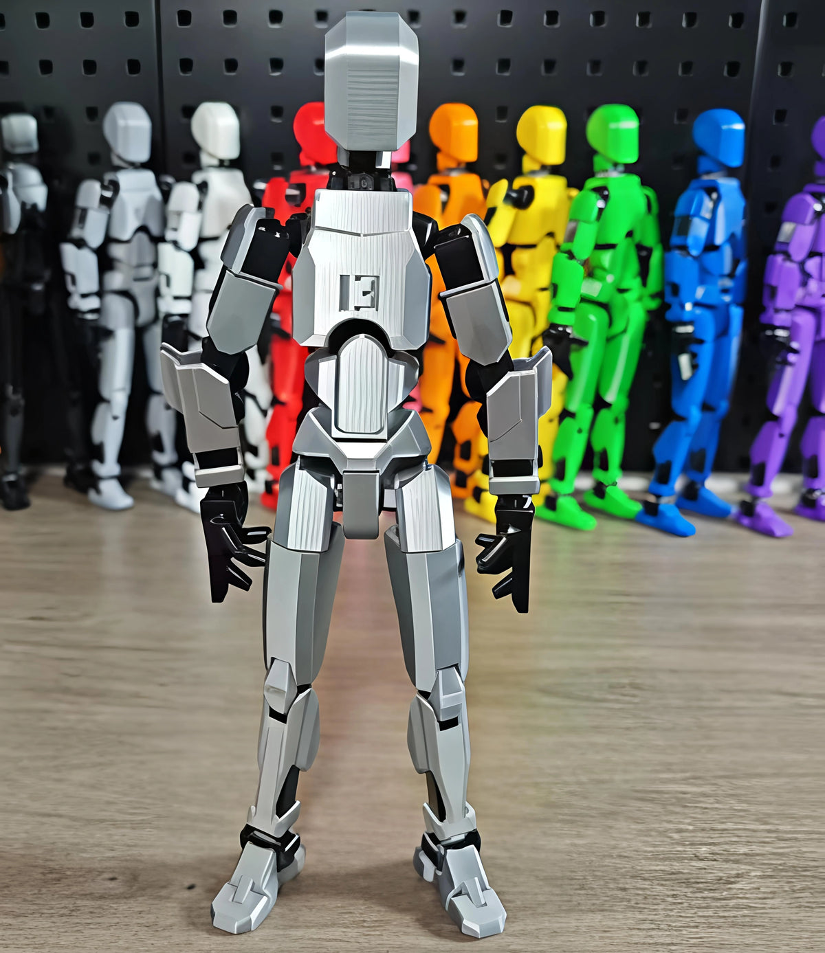 Toy robot figure with a gray and black color scheme, standing on a wooden surface with other colorfully painted robots in the background.