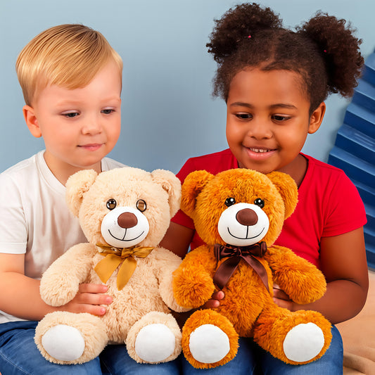 Two American children smiling and holding Giggly Groves 14" Small Teddy Bears—one cream-colored with a golden ribbon, the other orange-brown with a dark brown ribbon. The ultra-soft plush toys feature white muzzles, round noses, and white paw pads, creating a cozy and heartwarming indoor scene perfect for showcasing stuffed animal gifts for kids.